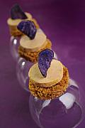Toasts ronds de pain d’épices surmontés de foie gras et d’une chips de pomme de terre vitelotte sur fond violet.