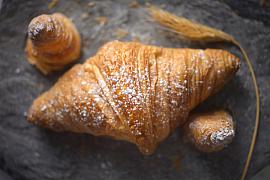 Croissant doré au sucre glace sur ardoise sombre avec un épi de blé.