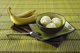 Trois boules de glace à la banane dans un bol sombre posé sur un set en bambou vert avec deux bananes entières.