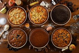 Vue de haut de six tartes sucrées sur bois avec farine œufs chocolat et fruits frais en décor culinaire.