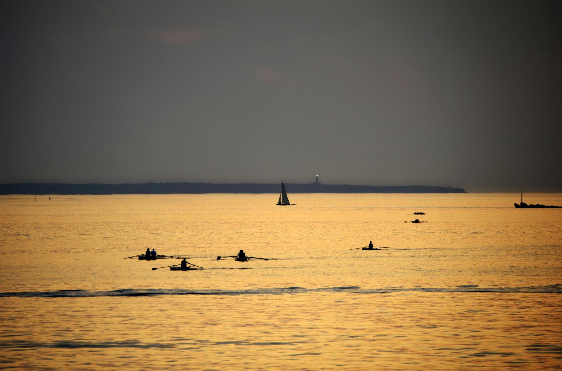 Silhouettes de plusieurs avirons naviguant sur une mer calme et dorée par le coucher de soleil à Saint-Malo