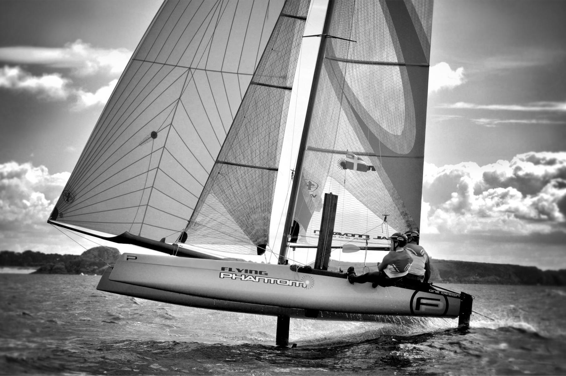 Photographie Photographe nautique et voile, je capte l'immersion au cœur d'une régate avec un Flying Phantom volant au-dessus des vagues. Une œuvre en noir et blanc illustrant la beauté des bateaux volants au dessus de l'eau