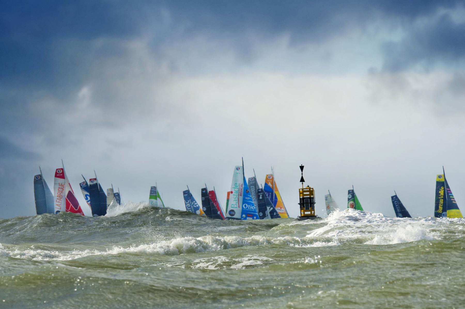 Photographie Photographe nautique et voile, je capte l'immersion au cœur du départ de la Transat au Havre. Les monocoques IMOCA défient une mer agitée, capturant l'essence de la compétition nautique.