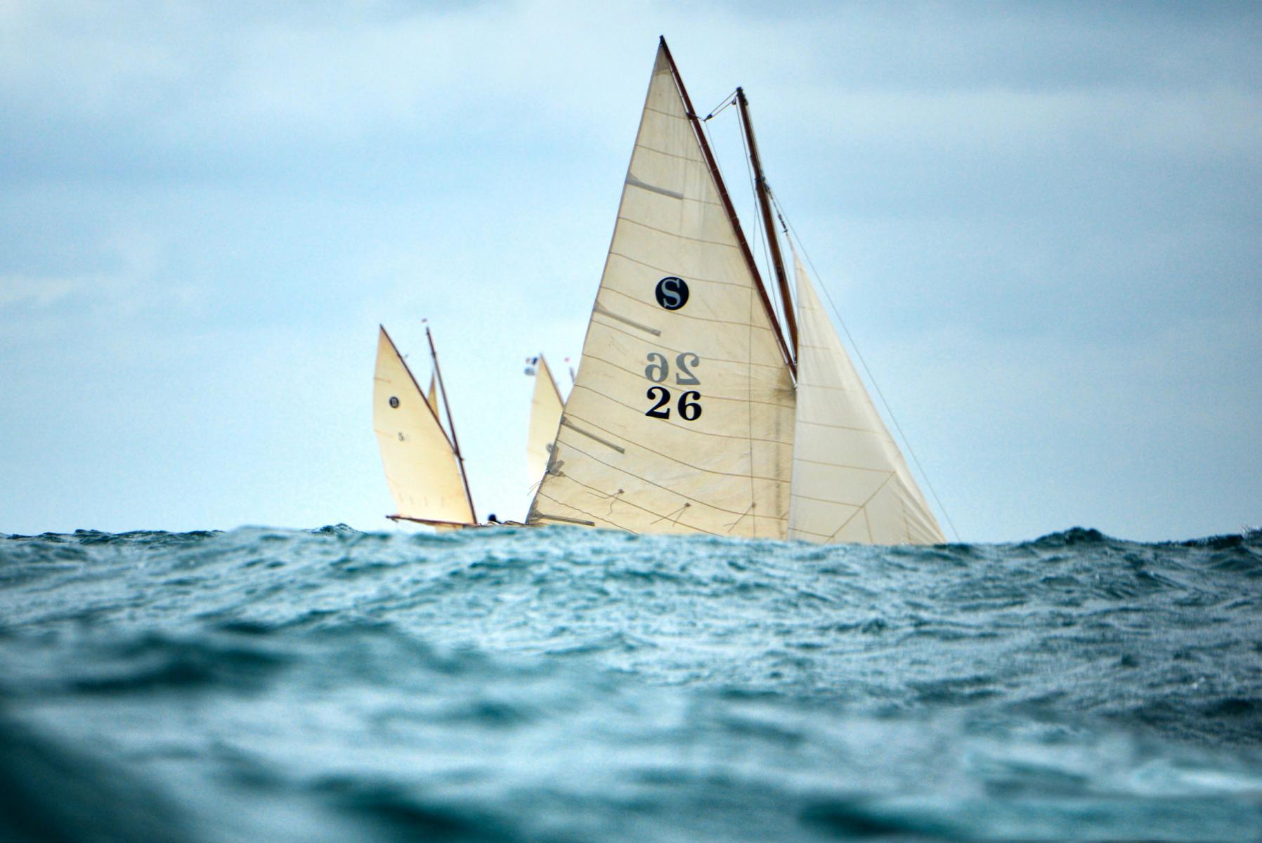 Photographie Photographe de la Bretagne, des voiliers et paysages marins, je capte le cœur d'une régate de vieux gréements en Bretagne. Cette prise de vue au ras de l'eau souligne la puissance des voiles classiques.