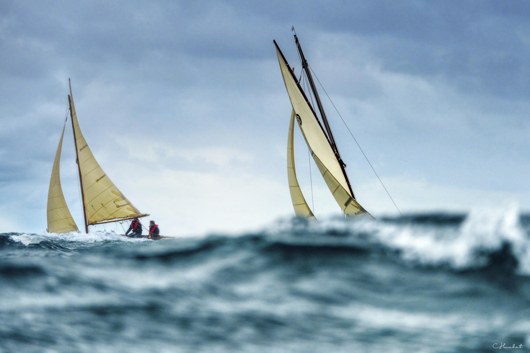 Deux vieux gréements aux voiles jaunes naviguant dans une houle sombre et agitée sous un ciel nuageux en Bretagne.