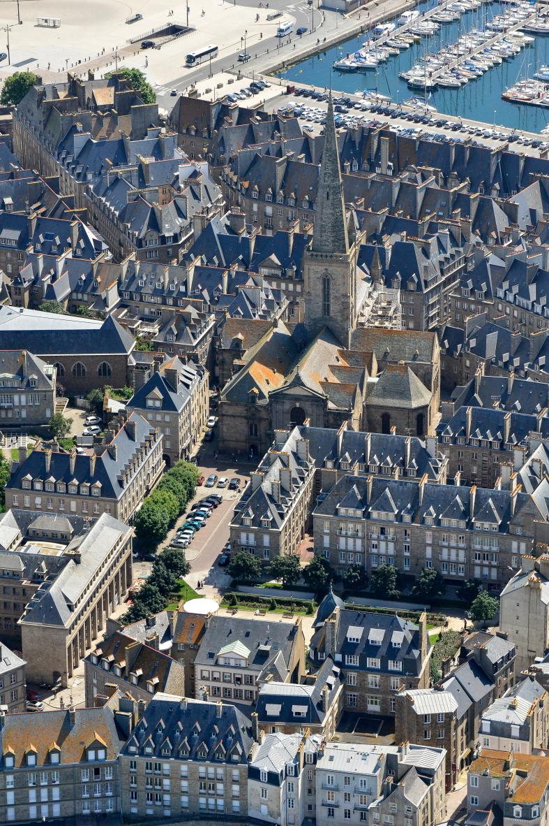 Vue aérienne des toits de Saint-Malo entourant la flèche de la cathédrale Saint-Vincent avec le port de plaisance au fond.