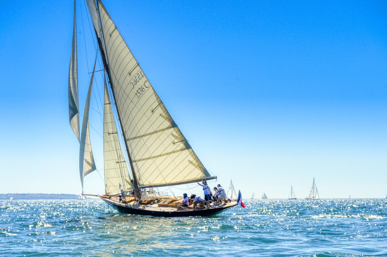 Voilier classique Pen Duick naviguant sous voiles blanches sur mer bleue scintillante sous un franc soleil breton.