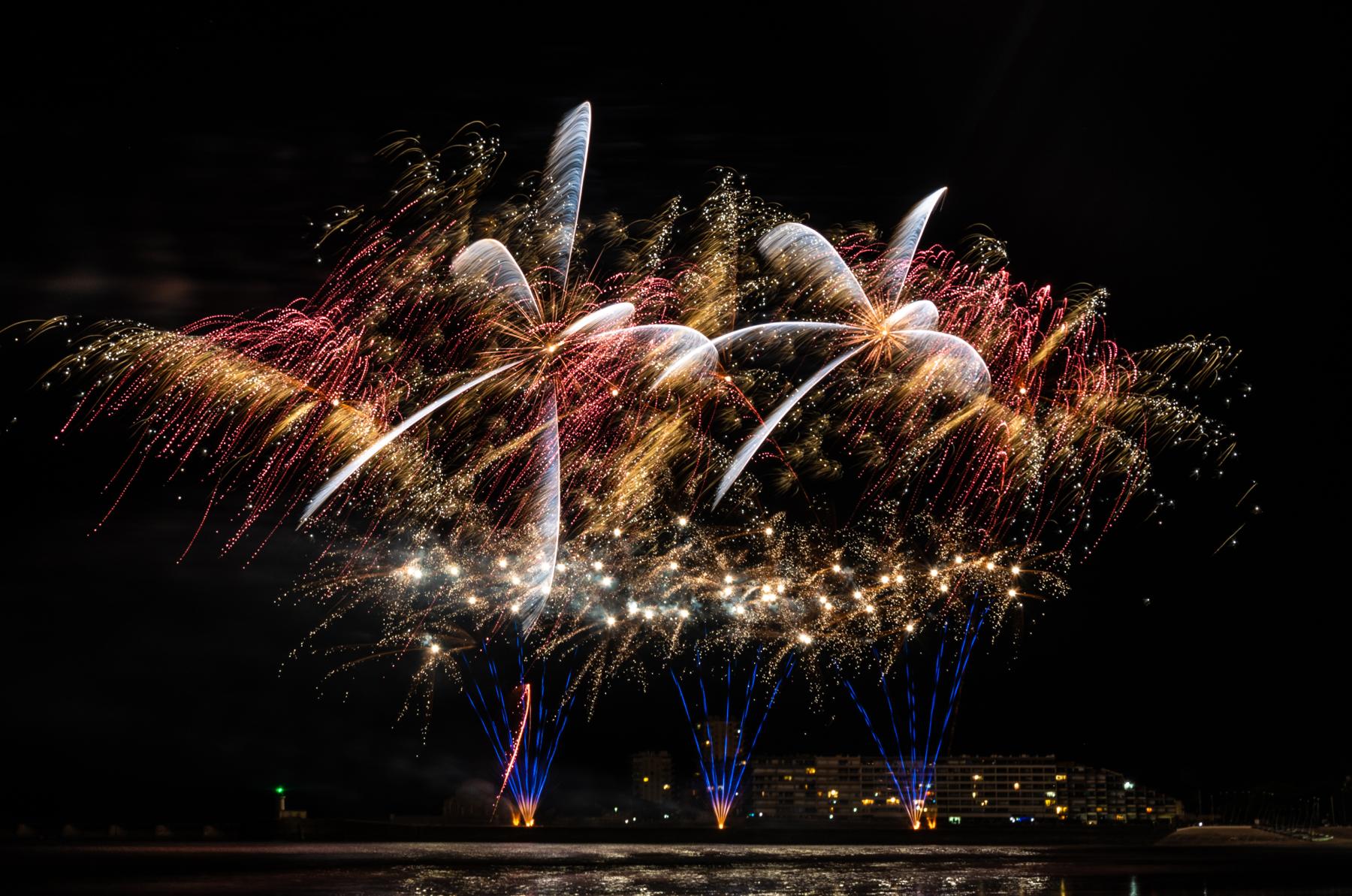 Explosions pyrotechniques dorées et rouges au-dessus de l’eau aux Sables d’Olonne en pleine nuit