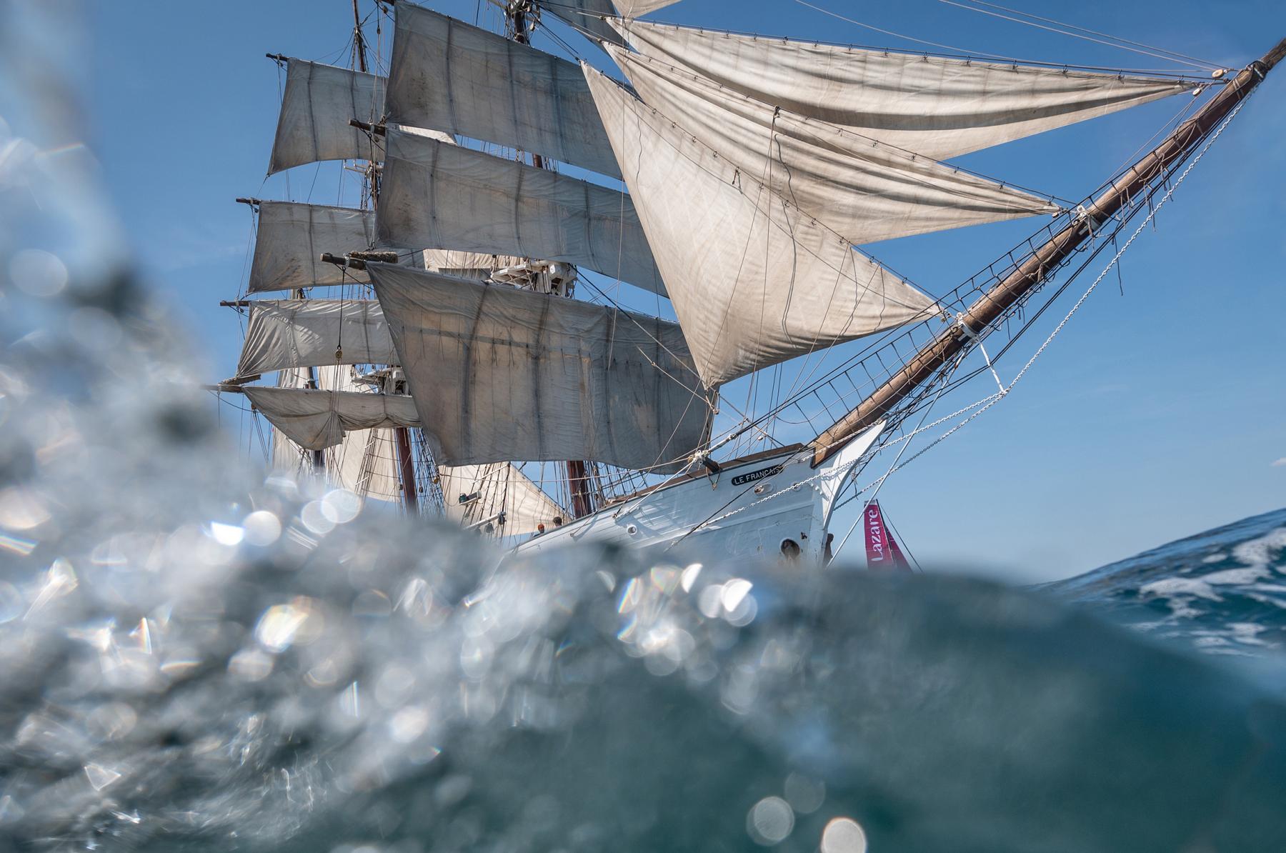 Photographie Photographe nautique et voile, je capte la Grande Armada Lazare : rencontre entre le vieux gréement Le Français et l'Imoca Lazare sous un ciel azur.